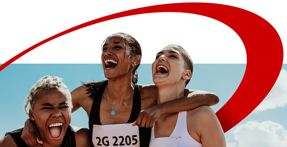 Three female athletes in race bibs celebrate joyfully with arms around each other after finishing a race.