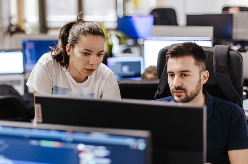 Two focused software specialists work closely together on a computer screen.
