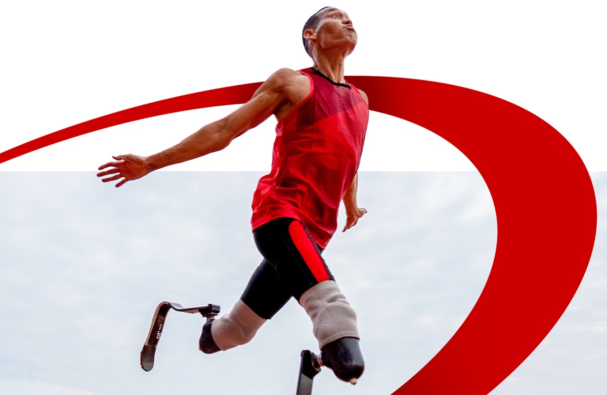 A male athlete with blade prosthetics sprints mid-air in a red outfit.