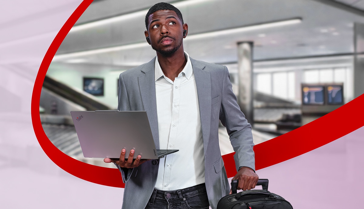 Man walking through an airport holding a Lenovo laptop.