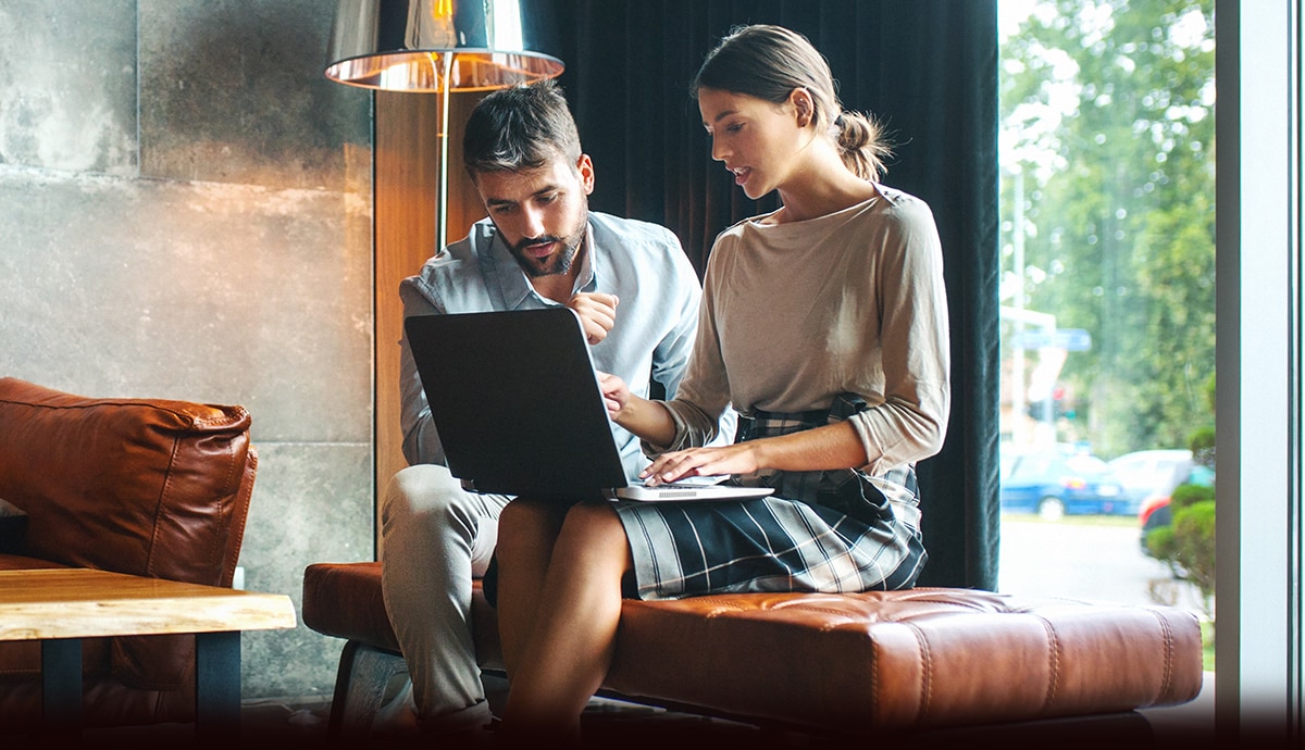 A male and female collaborating on a laptop in a lounge.