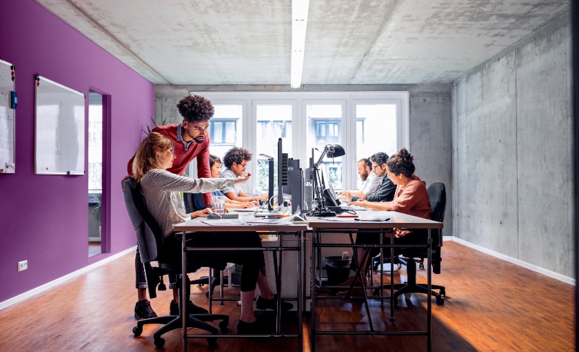 An office setting with employees collaborating and working on their computers.