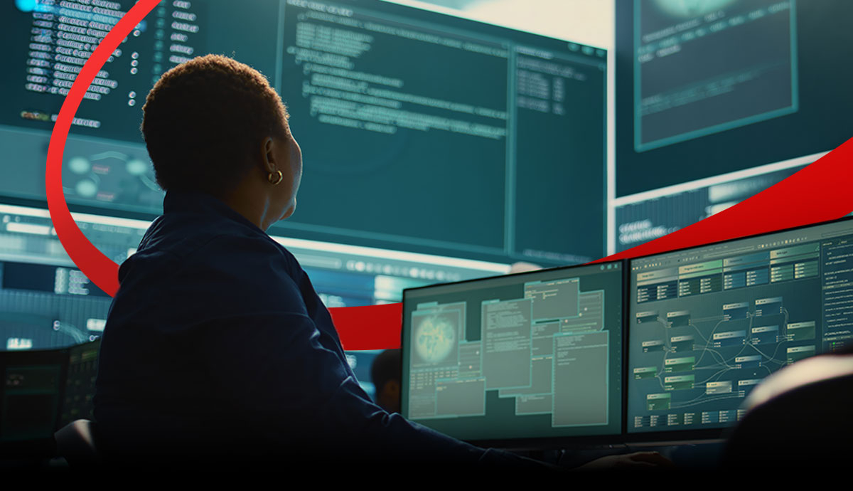 Person operating multiple computer monitors showing software and monitoring dashboards in a dark technology operations workspace, with a red curved graphic element in the background.
