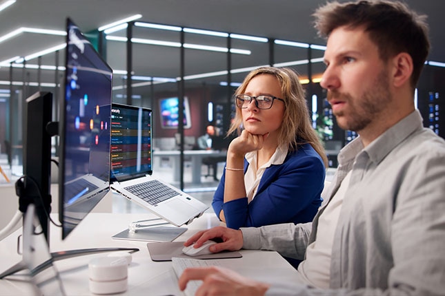 Two professionals monitoring security dashboards at workstation in operations center