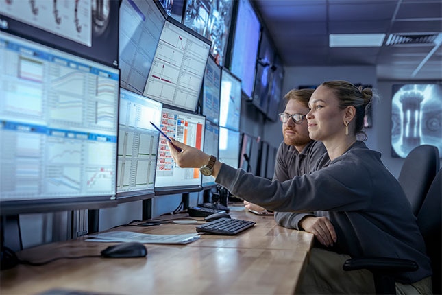 Two people reviewing data dashboards on multiple monitoring screens
