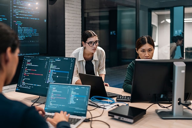 Team members reviewing code and system dashboards at computer workstations