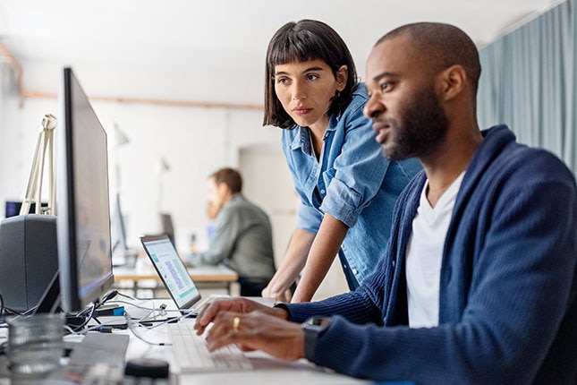 Two colleagues reviewing information together at desktop workstation monitors