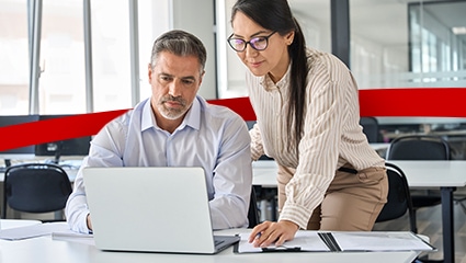 Two coworkers collaborating in bright office on laptop.