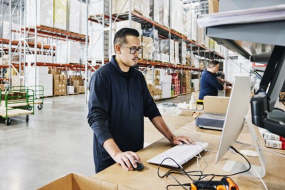 Warehouse worker checking orders at computer workstation in warehouse.