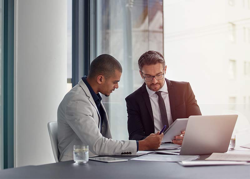 Two professionals analyzing reports on a laptop and tablet during a server and infrastructure capacity planning discussion.