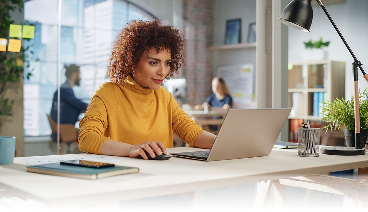 banner image of a woman working on a laptop computer at an office desk