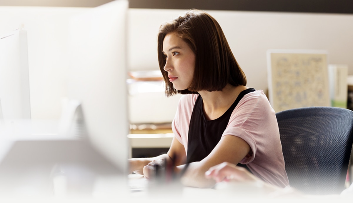 Woman working in front of a desktop computer in an office setting.
