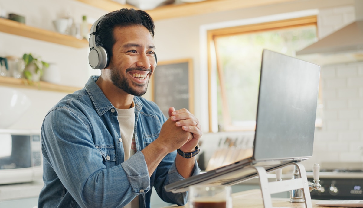 lifestyle hero image of a man working remote from home on a laptop computer wearing headphones.