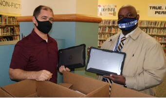 Two men wearing masks pose with computur tablets