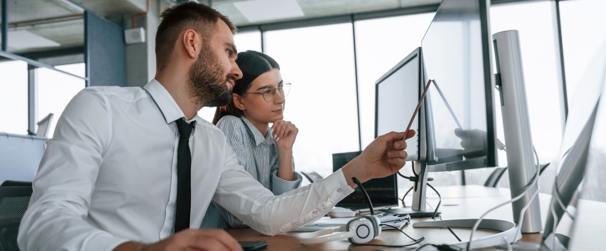 Two colleagues review data on a desktop monitor in a modern office setting.