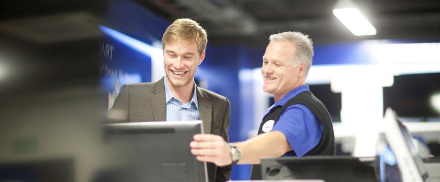 Two people review a portable computer together in an electronics showroom during a technology consultation.