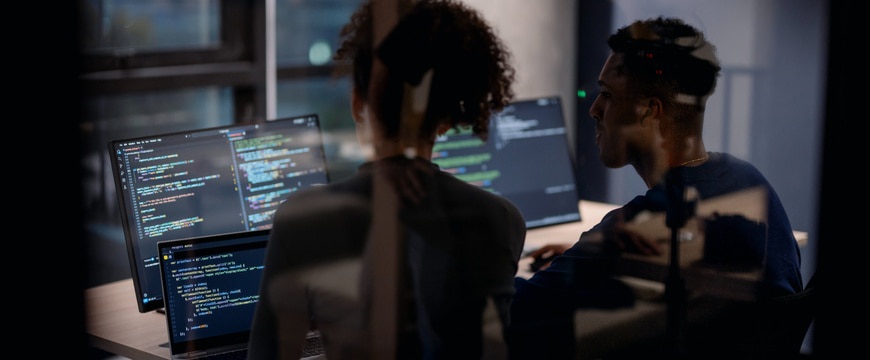 Two professionals working at multiple monitors displaying software code