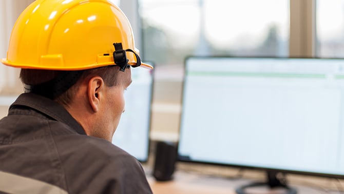 Man wearing hardhat looking at computer screen.