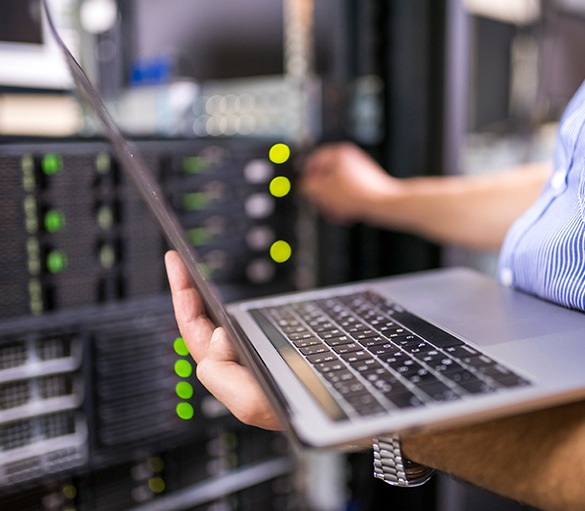 Close up image of a person holding a laptop and configuring a server.