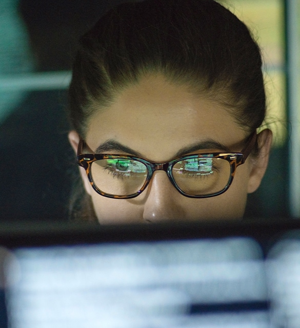 Close up image of a woman with glasses looking at computer screen.