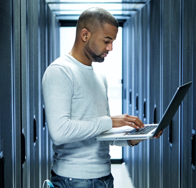 Image of man using laptop in server room.