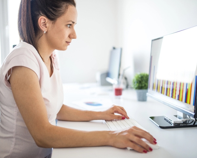 Close up image of a woman using keyboard and mouse while looking at computer screen.