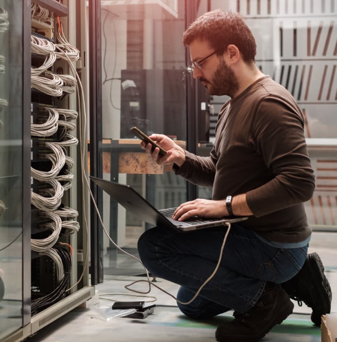 Image of man using laptop in server room.