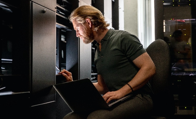 Image of man using laptop in server room.