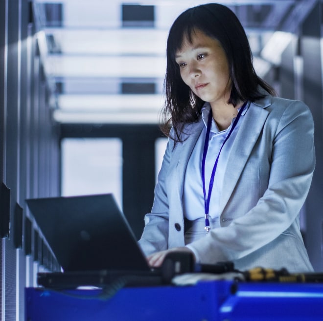 Image of woman using laptop in server room.