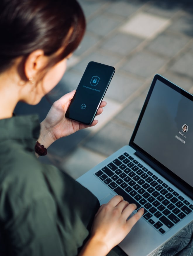 Image of a woman with a laptop using her phone for 2-factor authentication.