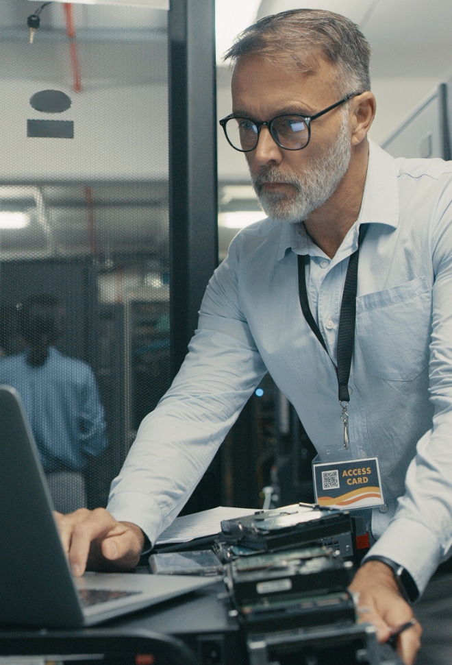 Image of a man in server room typing on laptop.