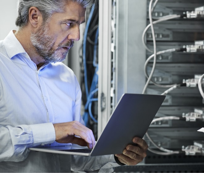 Close up image of a man using a laptop in a server room.