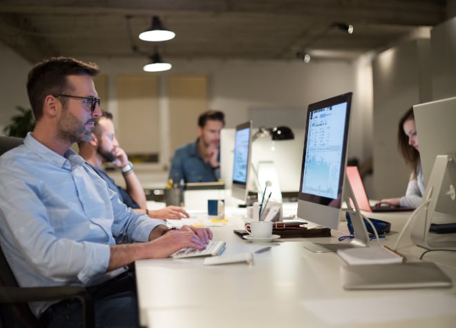 Image of a man sitting at desk looking at a display while typing on a keyboard.