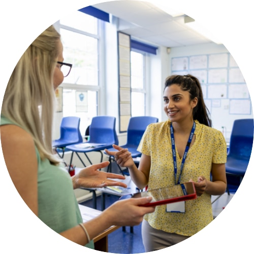 An over-the-shoulder view of two female teachers sharing teaching ideas with each other.