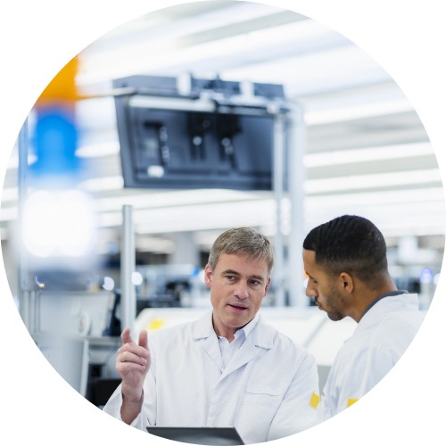 Technicians in lab coats discussing in electronics factory.