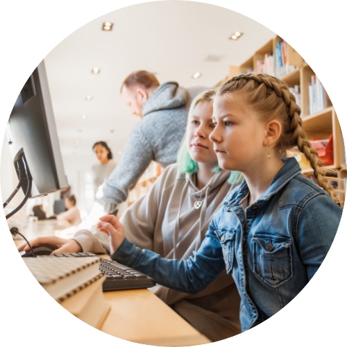 Two female students studying in a public library in front of a computer.