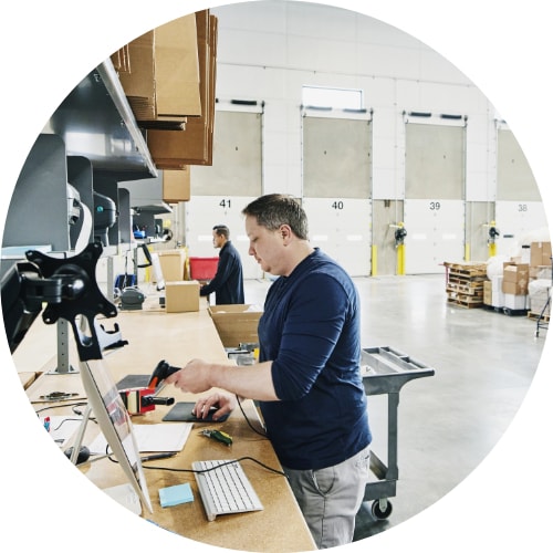 Shot of male warehouse worker scanning order sheet with bar code reader at computer in warehouse.