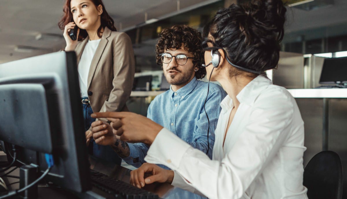 A team of IT professionals collaborates at a computer, with a female member pointing to something on the screen.