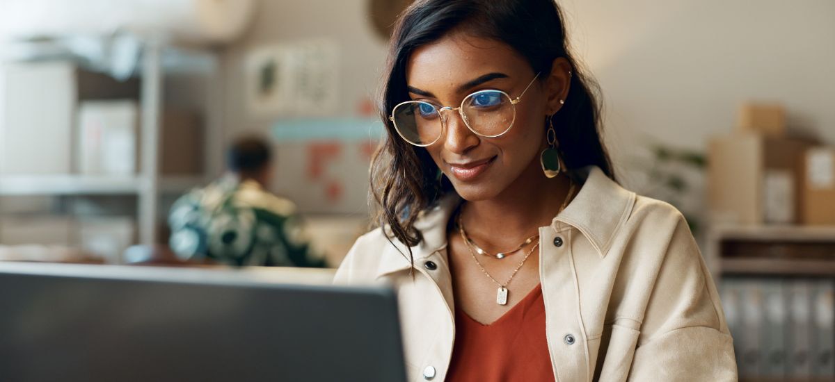 A young woman is smiling as she works on her computer.