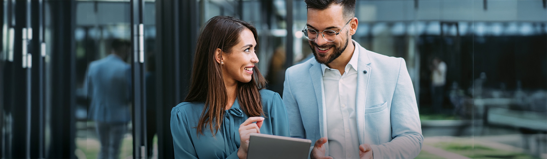 A man and a women standing outside an office looking at an IPad screen.