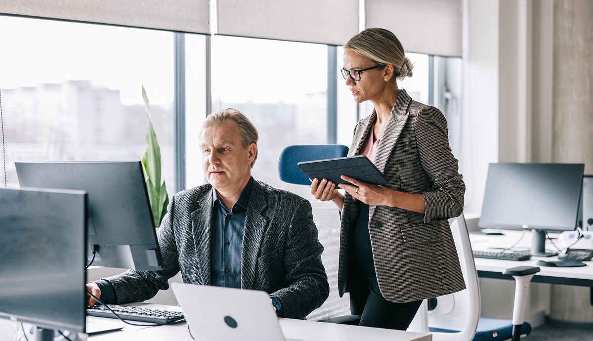 Coworkers collaborate at a desk surrounded by large office windows.