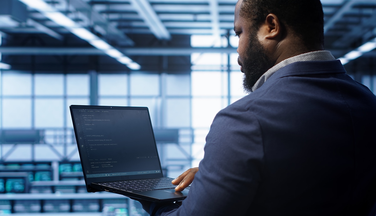 IT professional reviewing code on a laptop inside a modern, high-tech data center.