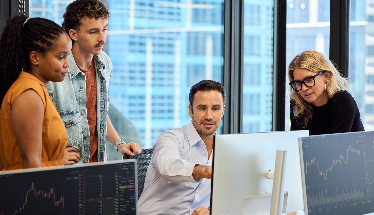 A team of four colleagues analyzes data on computer screens.