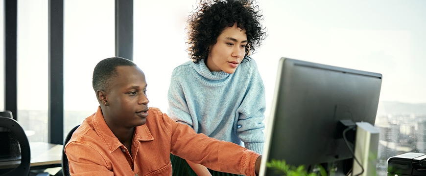 Coworkers working together on a computer in an office, discussing a project