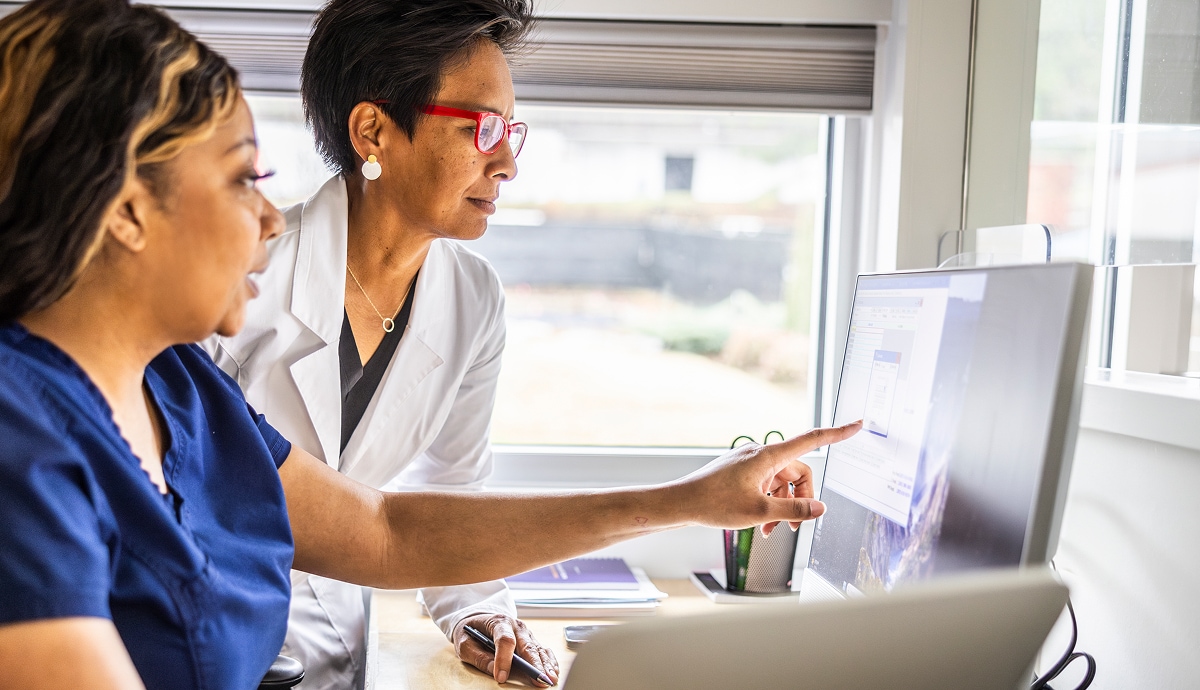 Healthcare professional reviewing information on desktop monitor with colleague.
