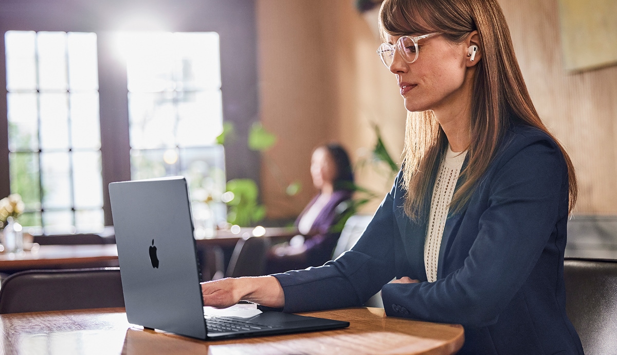 Professional working on a laptop with wireless earbuds in a modern workspace.