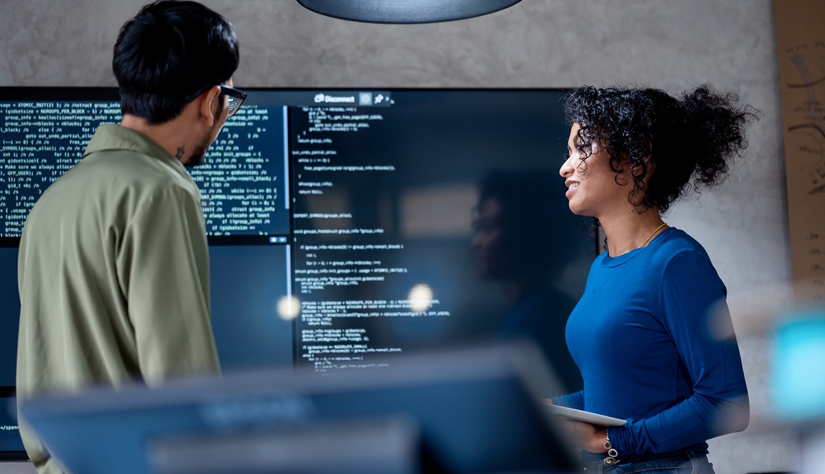 Software developers discuss code displayed on large monitors.