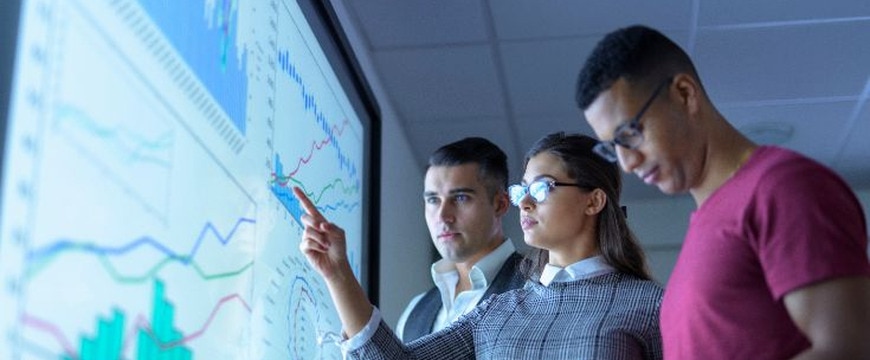 Three professionals reviewing data dashboard on large screen with charts and graphs