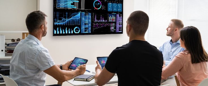 Team seated at table viewing data dashboards displayed on large screen