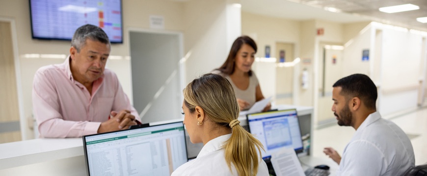 Reception staff work at computers while visitors review paperwork at counter